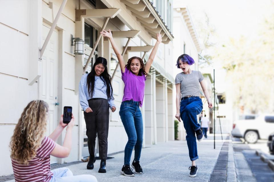 A person uses a smartphone to record three people dancing.