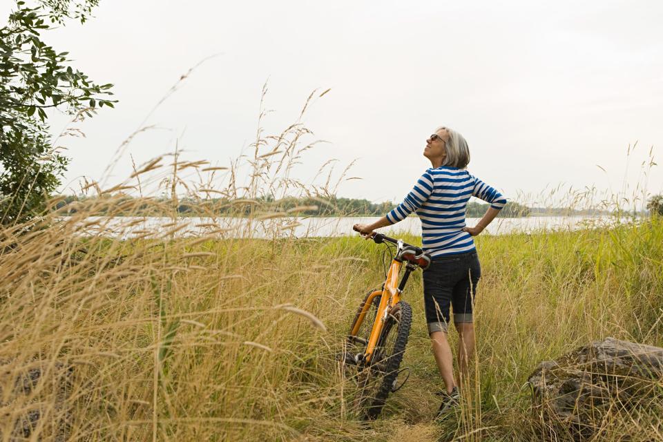 An older woman with a bike in a field.