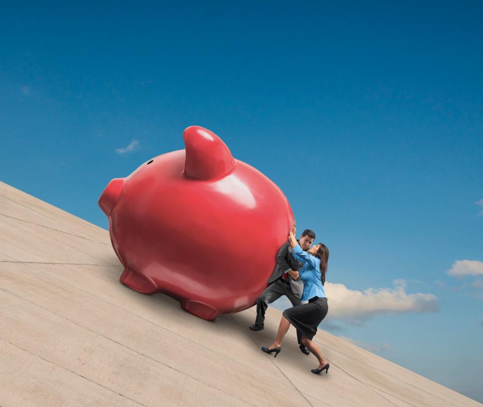 A couple pushing a huge piggy bank up a steep incline. 