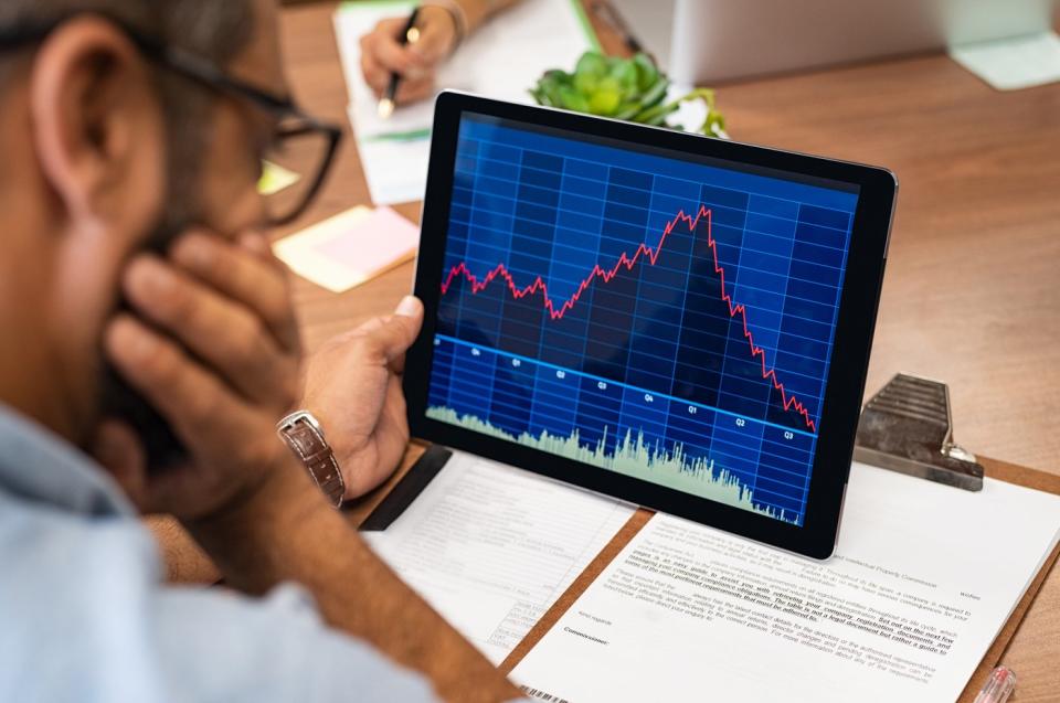 A visibly concerned person looking at a rapidly rising then plunging stock chart displayed on a tablet. 