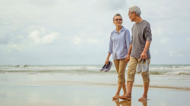 A recently retired couple walks on the beach and talks about their financial plan for retirement.