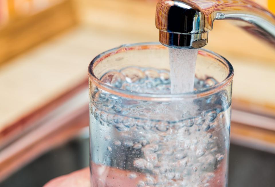 A person filling a glass of water using a kitchen faucet. 