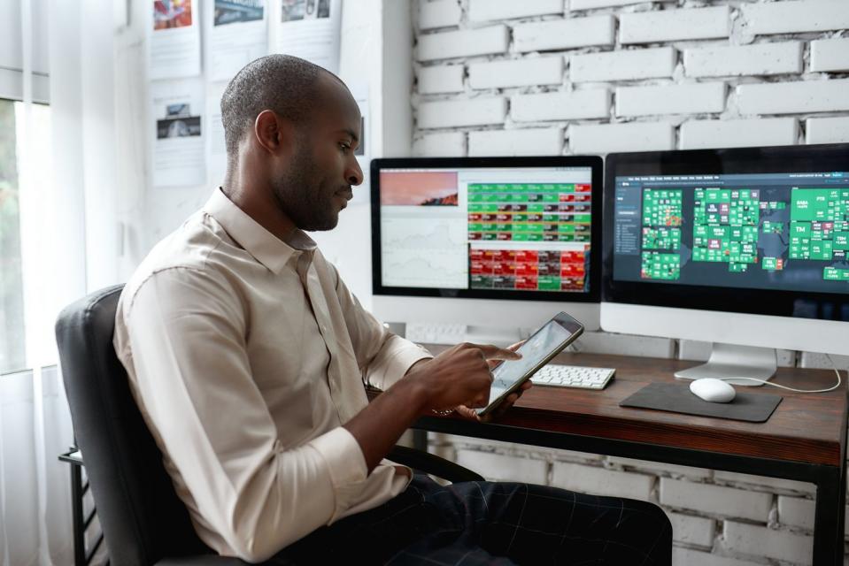 Person sitting at desk, stock screens on the desktop monitors, looking at phone.