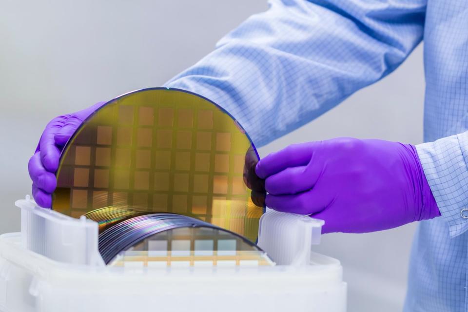 Technician handles circular semiconductor wafers. 