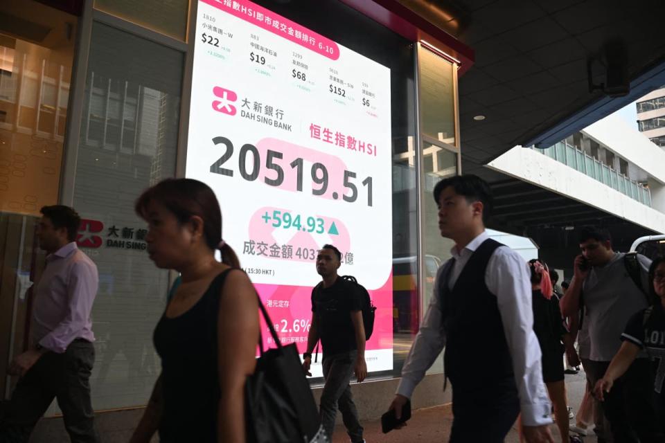 Pedestrians walk past a sign showing the numbers of the Hang Seng Index in Hong Kong on Sept. 27, 2024. 