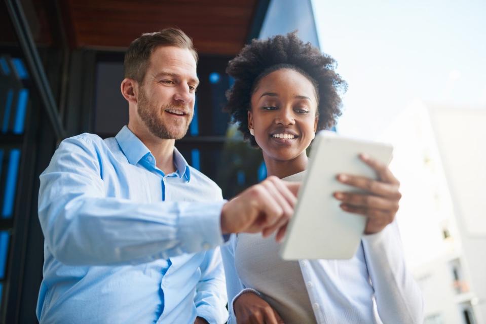 Two investors look at something on a tablet outdoors.