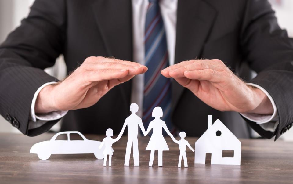 A businessperson placing their hands above paper cutouts of a family, a house, and a car.