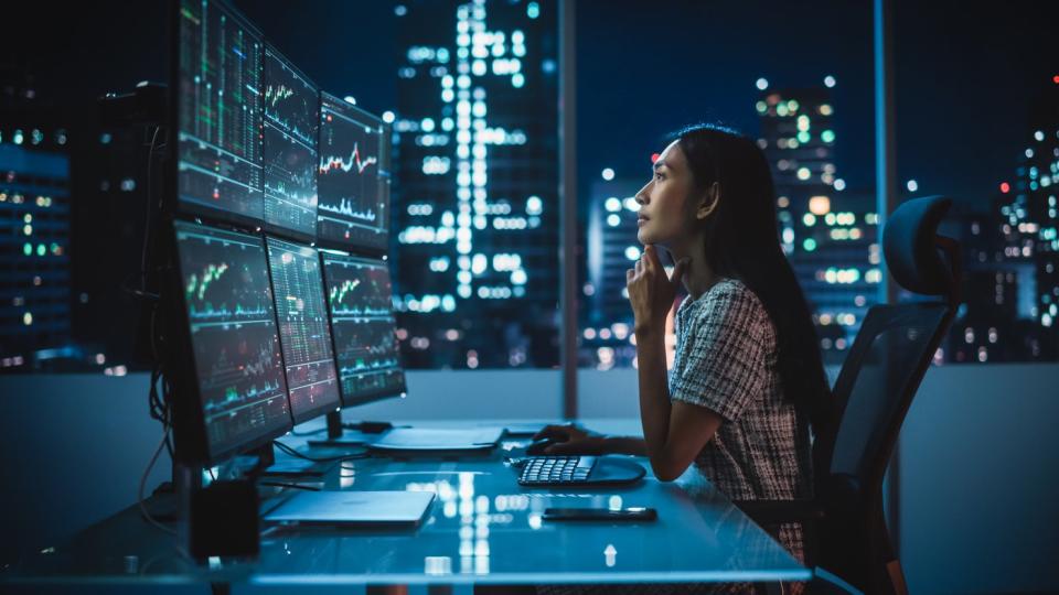 A hedge fund analyst looking at investment charts on computer monitors.