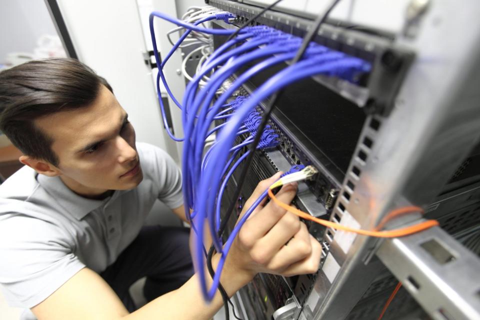 An engineer placing wires into the back of a data center server tower.