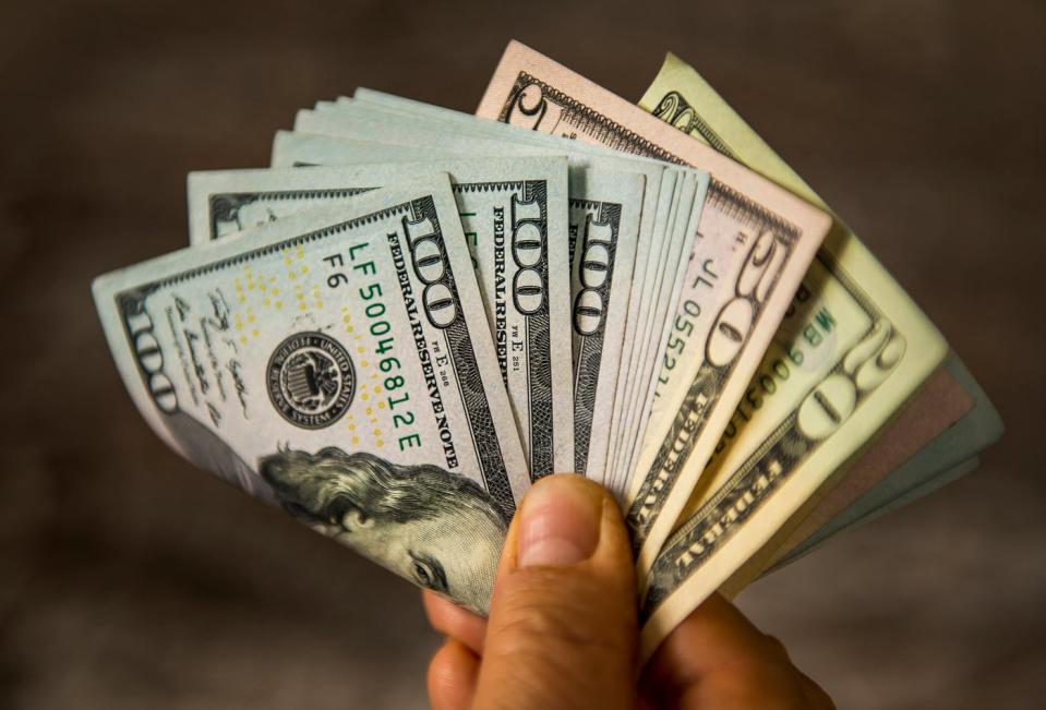 A person holding a fanned and folded assortment of cash bills in their hands. 