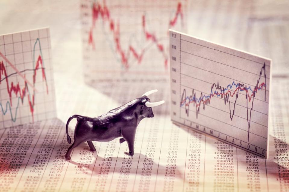 A bull figurine set atop a financial newspaper and in front of volatile pop-up stock charts. 