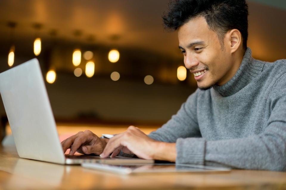 A businessperson typing on a laptop while seated inside of a cafe.