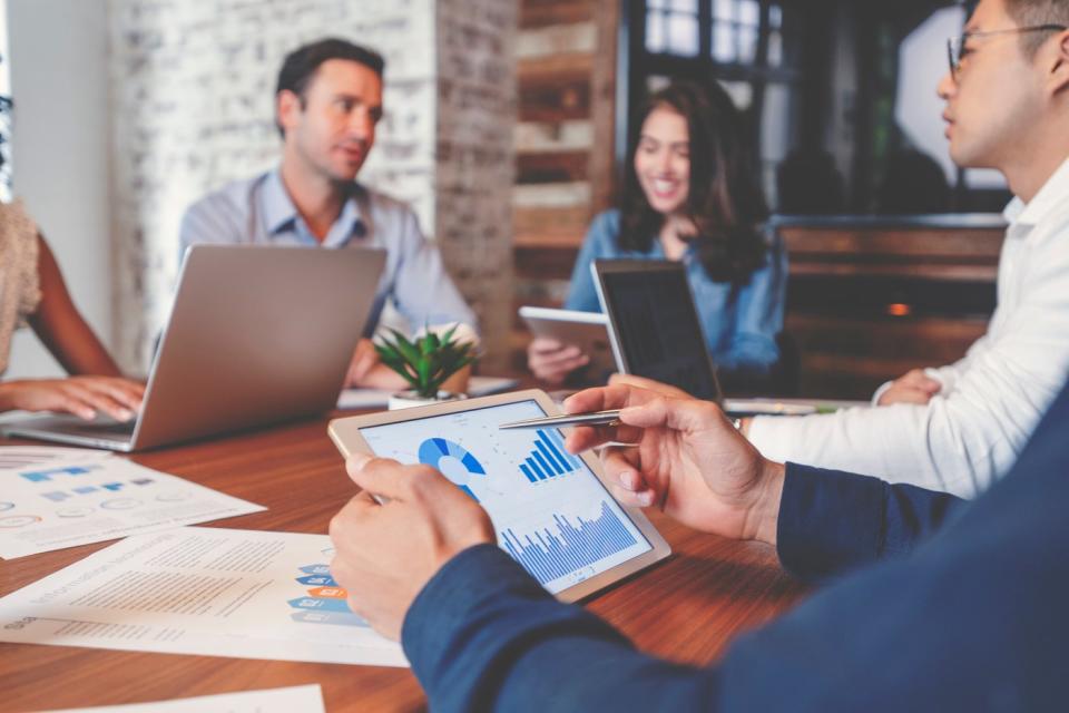 Employees using tablets and laptops to analyze business metrics while seated in a conference room.