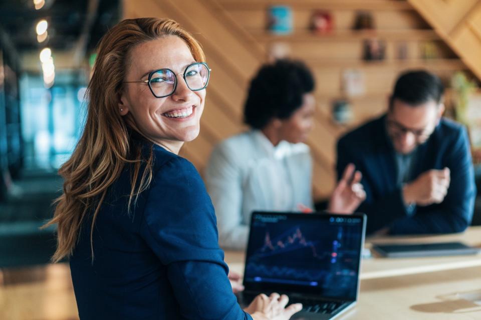 A happy stock trader works on a laptop in an office.