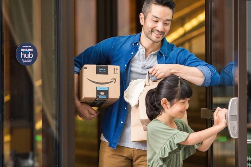 A parent holding an Amazon package under their right arm, with their child holding a door open for them.