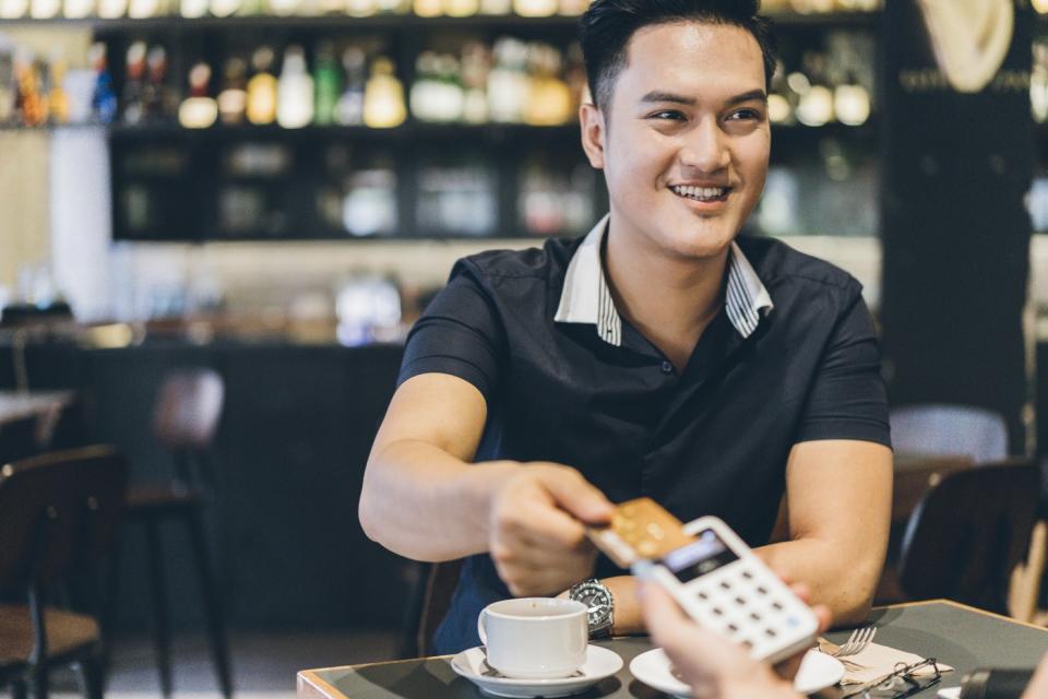 A person holding a credit card above a portable point-of-sale device inside a restaurant. 