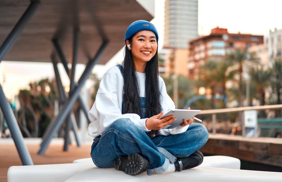 Some sitting on a chair while holding a tablet.