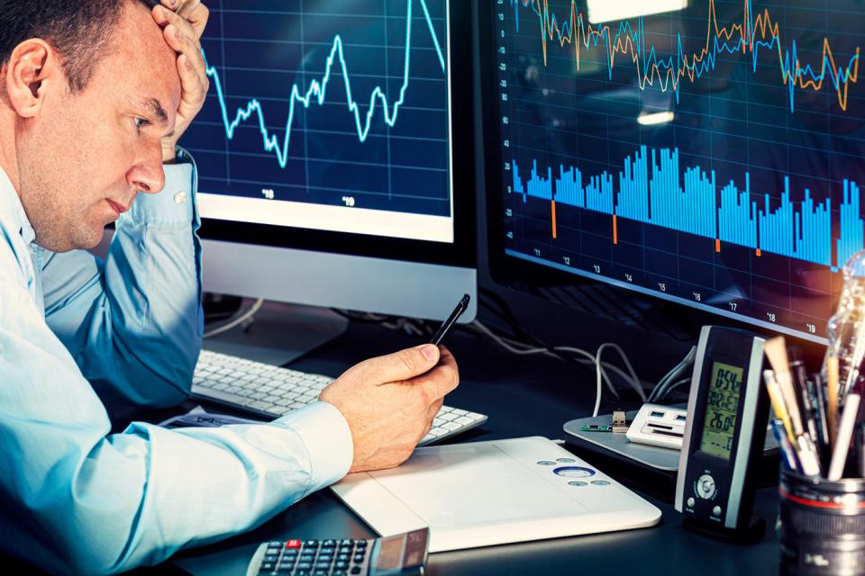 A money manager analyzing stock charts displayed on two computer monitors. 