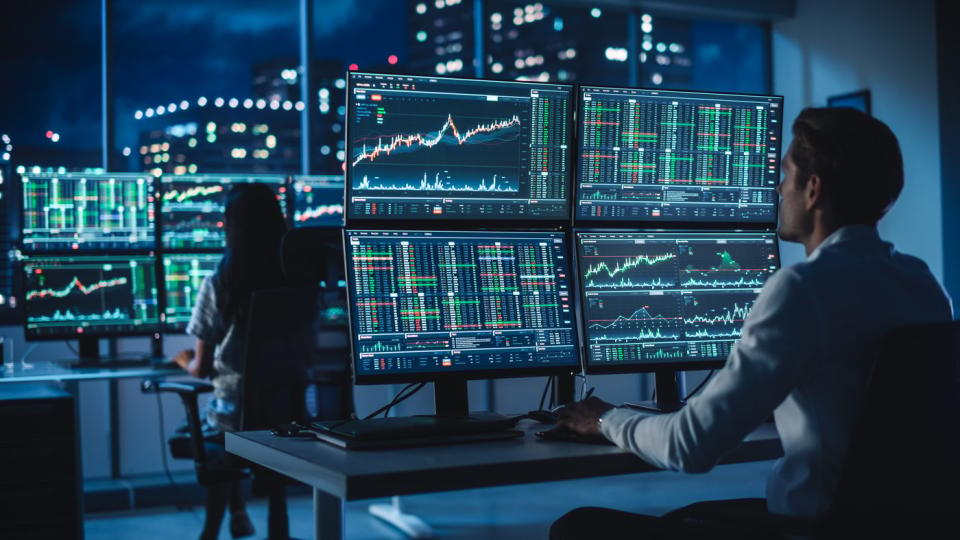 Two people looking at several monitors against an urban nightscape.