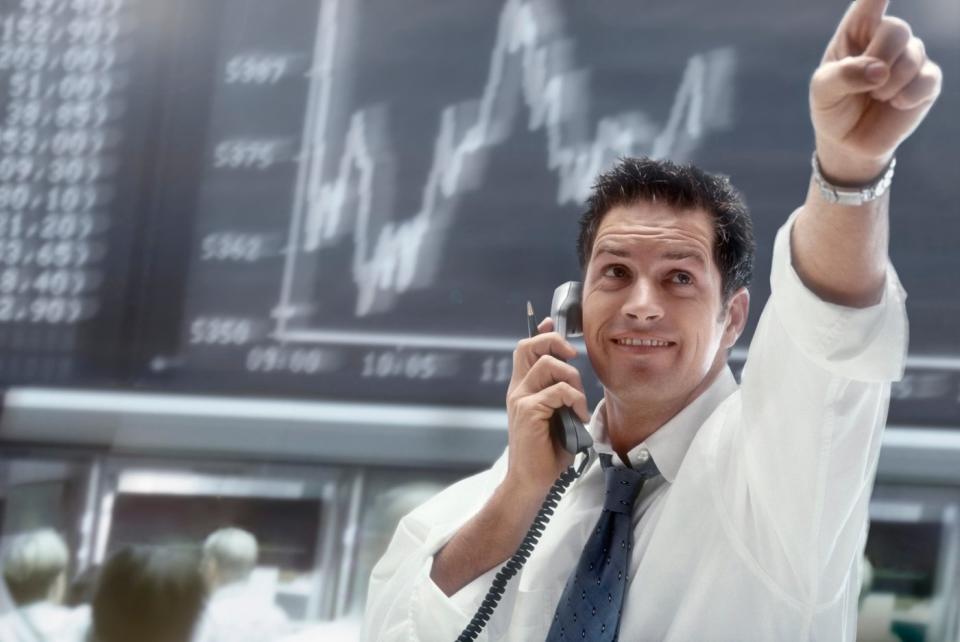 A person on the phone pointing to upward movement on a stock chart.