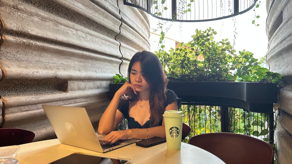 A young woman typing on her laptop with a Starbucks cup next to her.